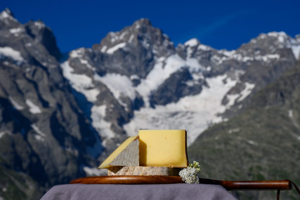 Cheese collection, French cow cheese comte, beaufort, abondance and snowy tops of french Aples mountains village in summer in Haute-Savoie on background